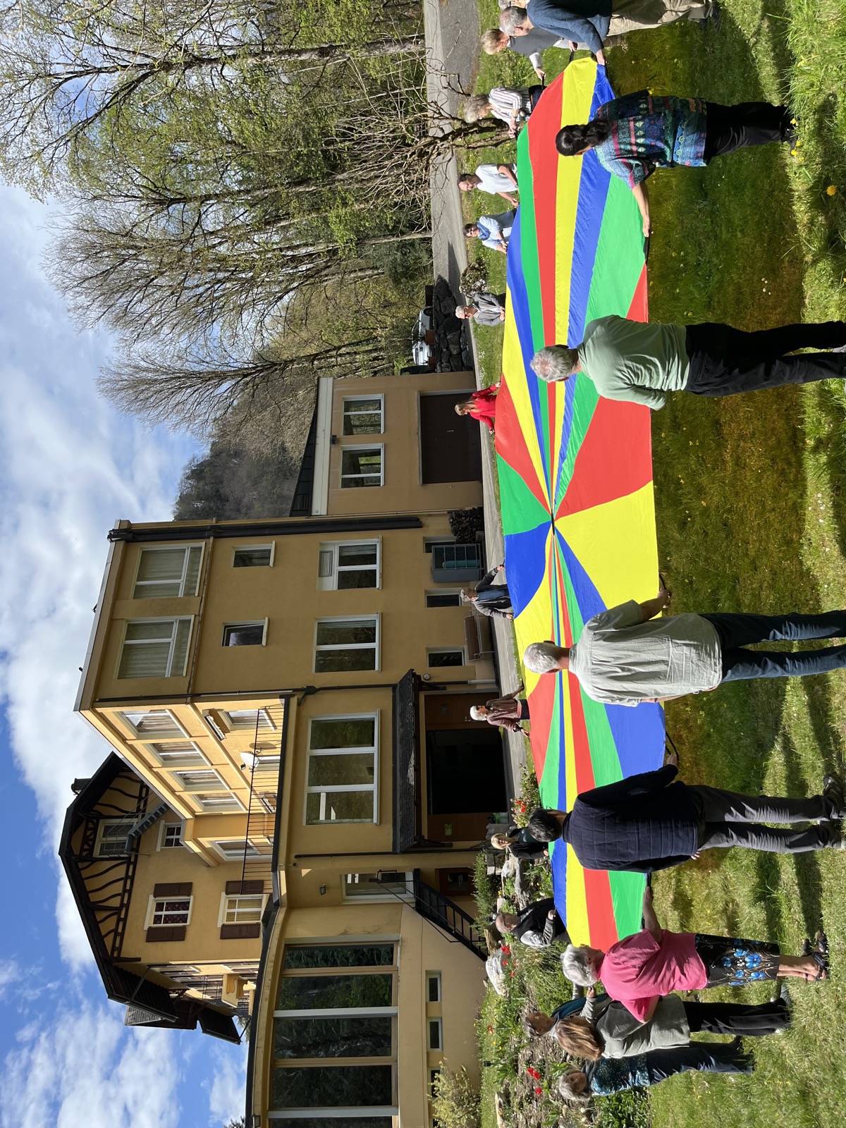 Enfants jouant avec un parachute coloré devant le Foyer de Charité