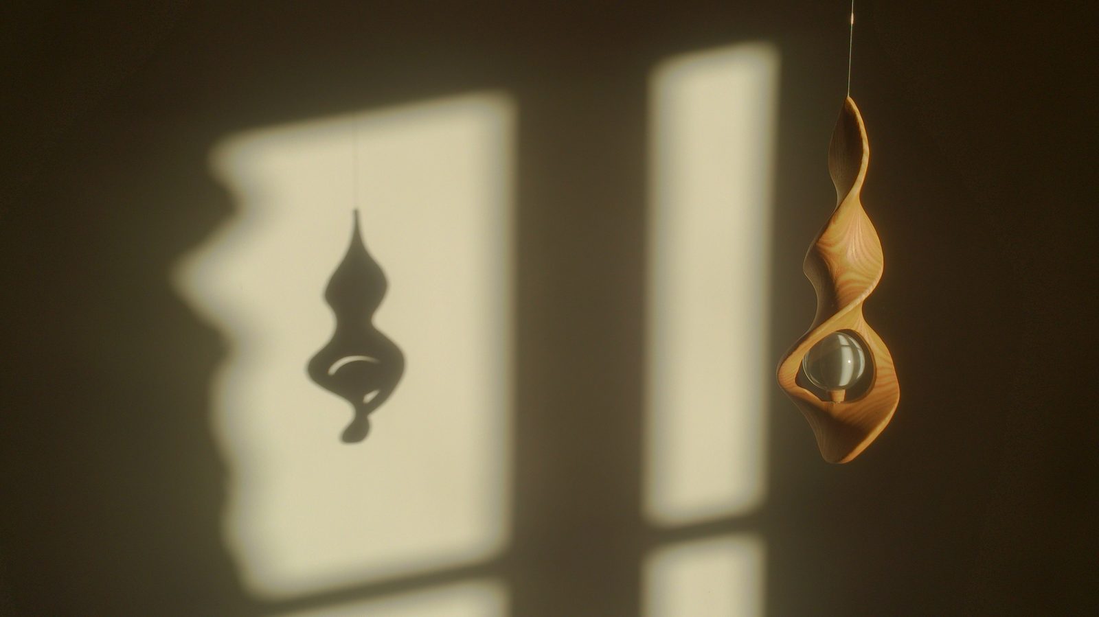Sculpture en bois suspendue et son ombre projetée par la lumière de la fenêtre, chapelle du Foyer
